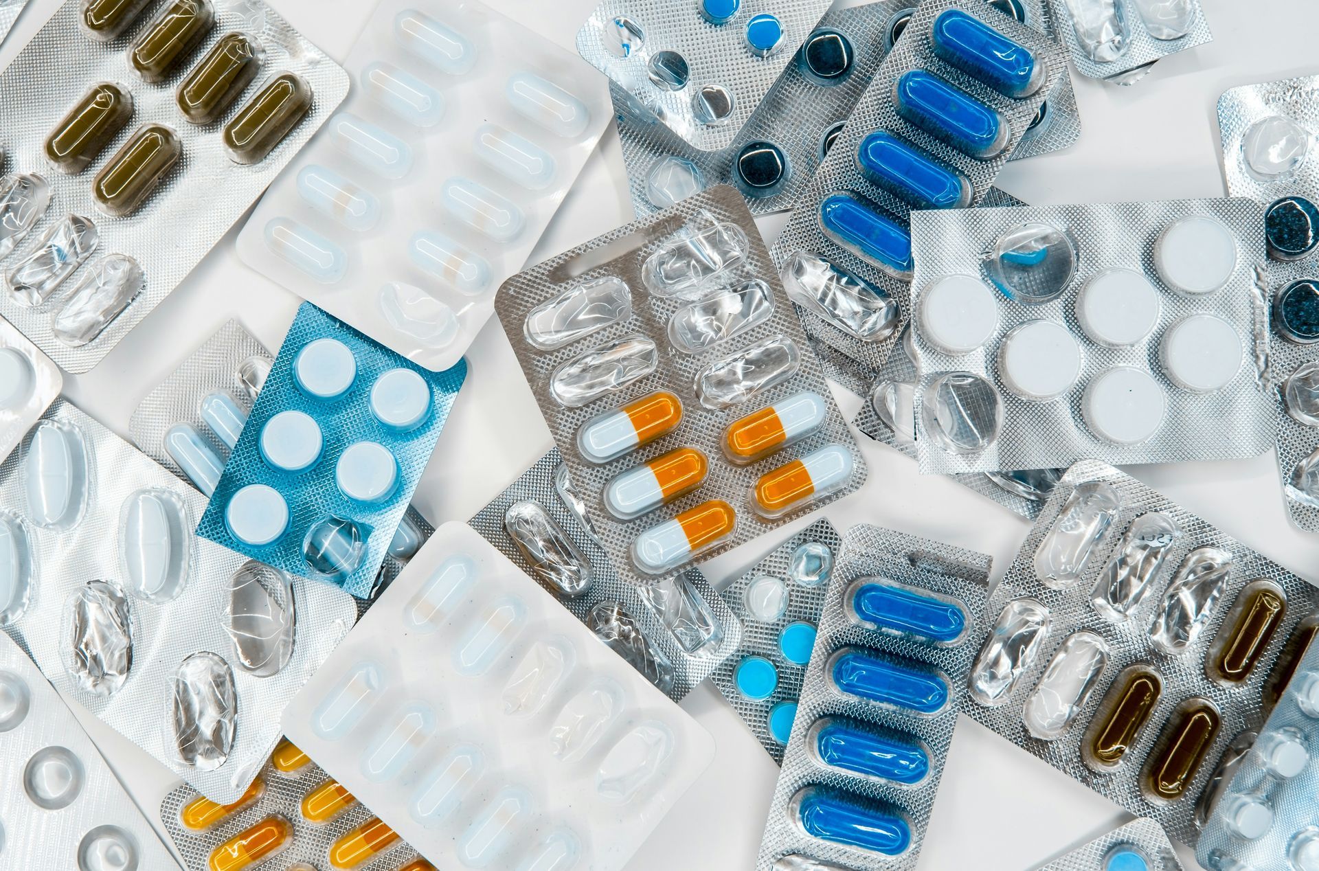 A variety of colorful prescription pills and capsules in blister packs scattered across a surface.