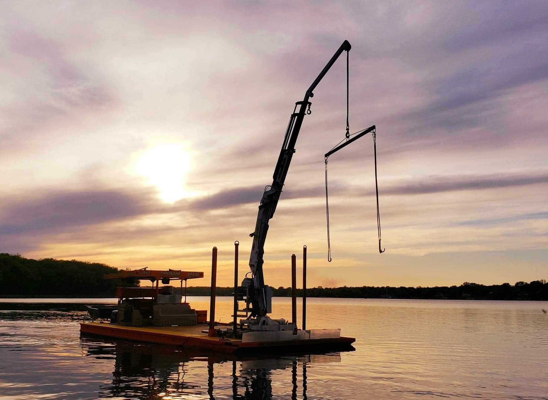 A boat with a crane attached to it is in the water at sunset