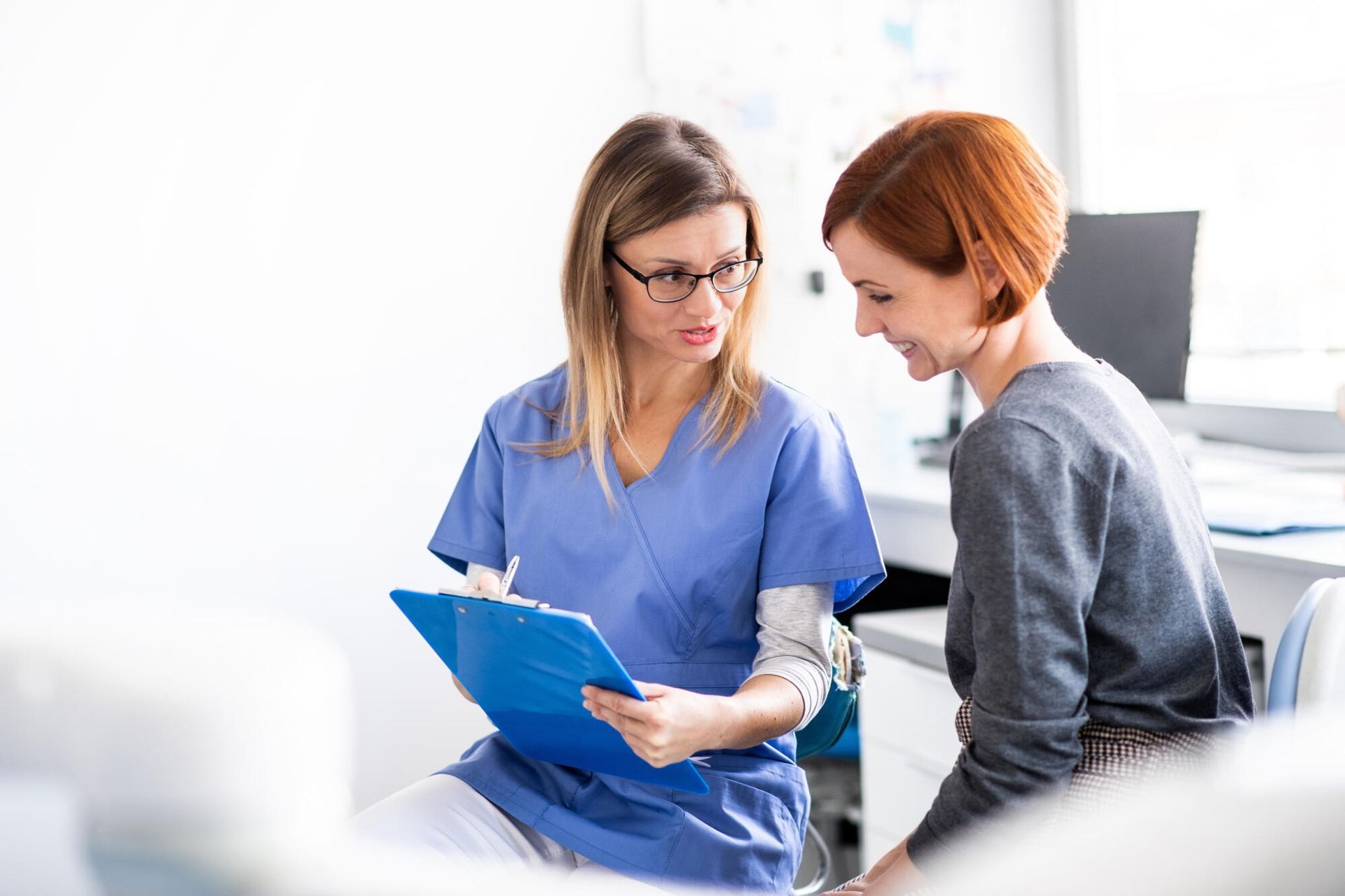 A nurse is talking to a patient while looking at a clipboard.