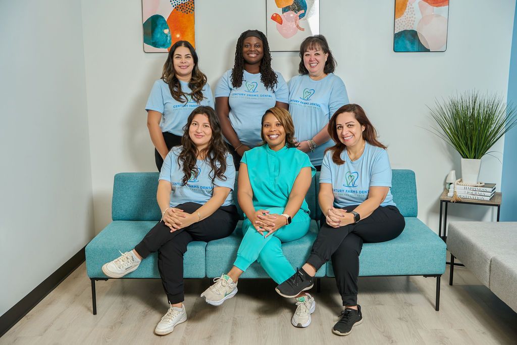 Group of women in matching blue shirts and turquoise scrubs pose on a blue couch in a brightly lit room.