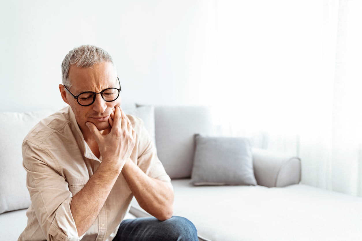 A man wearing glasses is sitting on a couch with his hands on his chin.