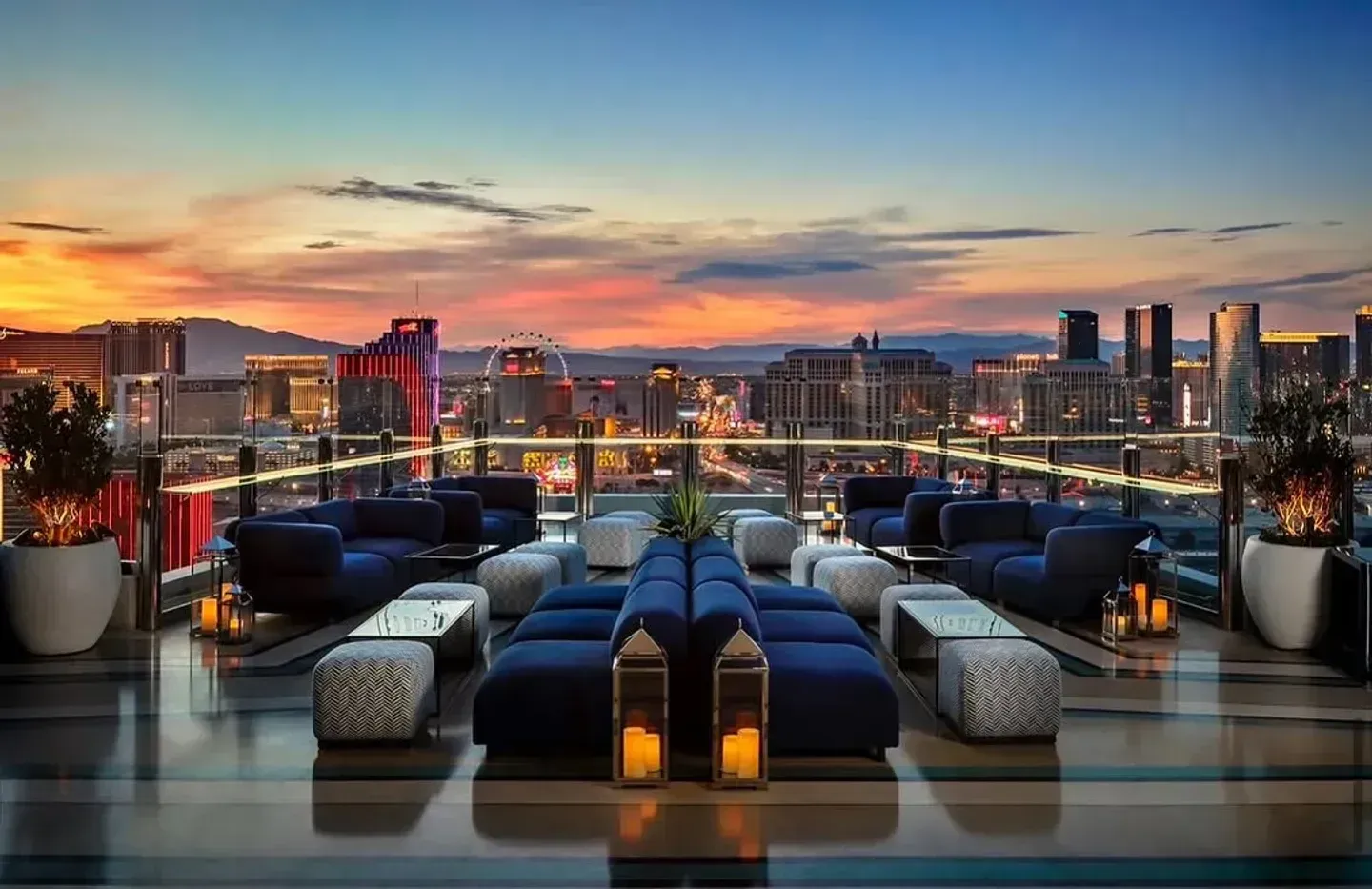 A rooftop lounge at sunset overlooking the Las Vegas skyline with blue sofas, low tables, and glowing lanterns.