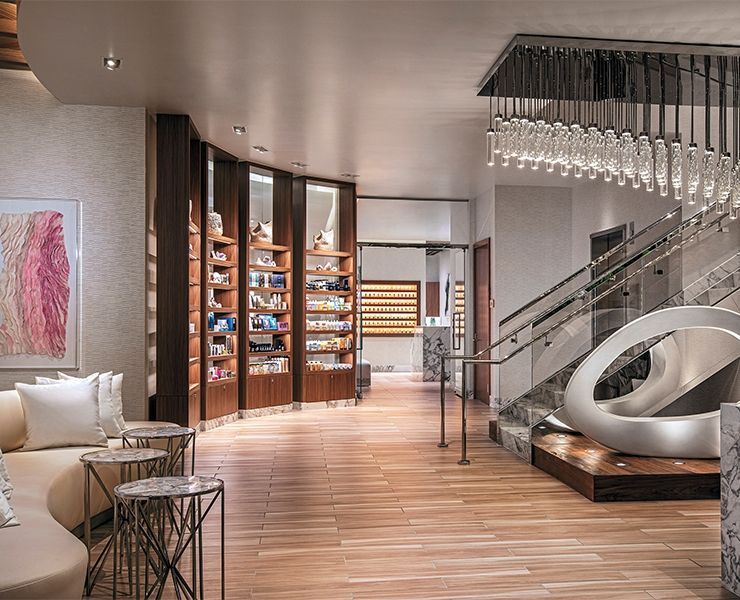 Lobby area with wood flooring, retail shelving, modern light fixtures, a white sofa, and a staircase with glass railings.