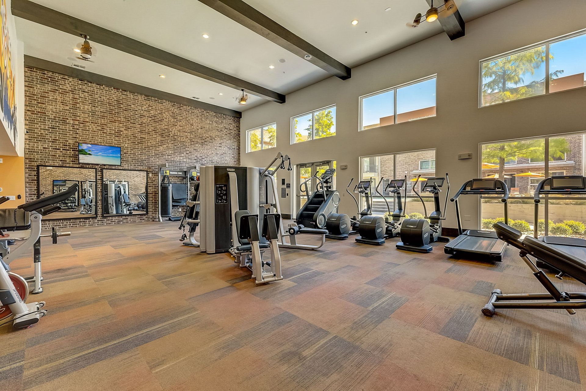 Gym interior with weight machines, treadmills, and windows, in a well-lit space with neutral colors.