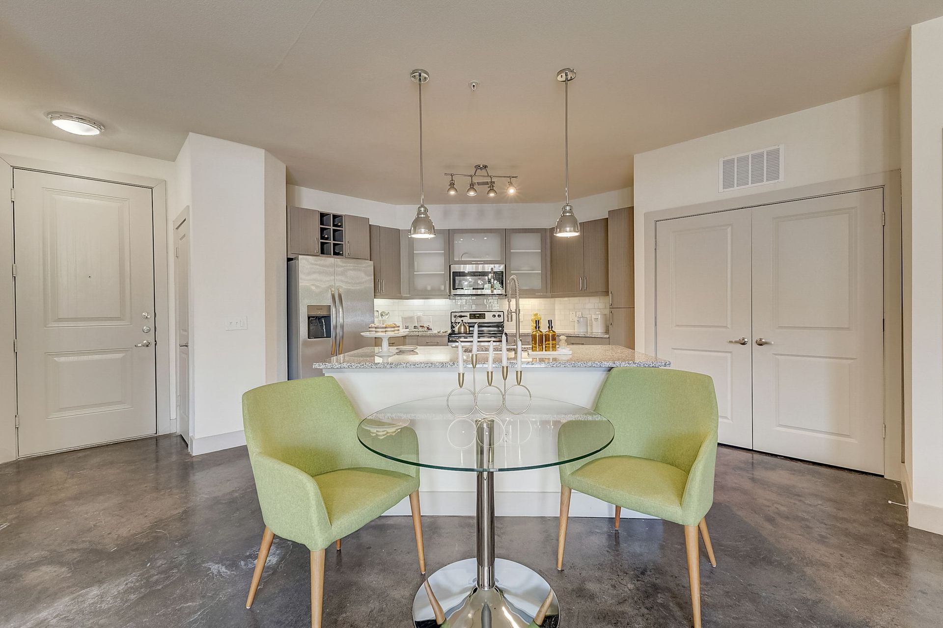 A modern kitchen with a small dining table and two lime-green chairs. Polished concrete floors and light-colored cabinets.