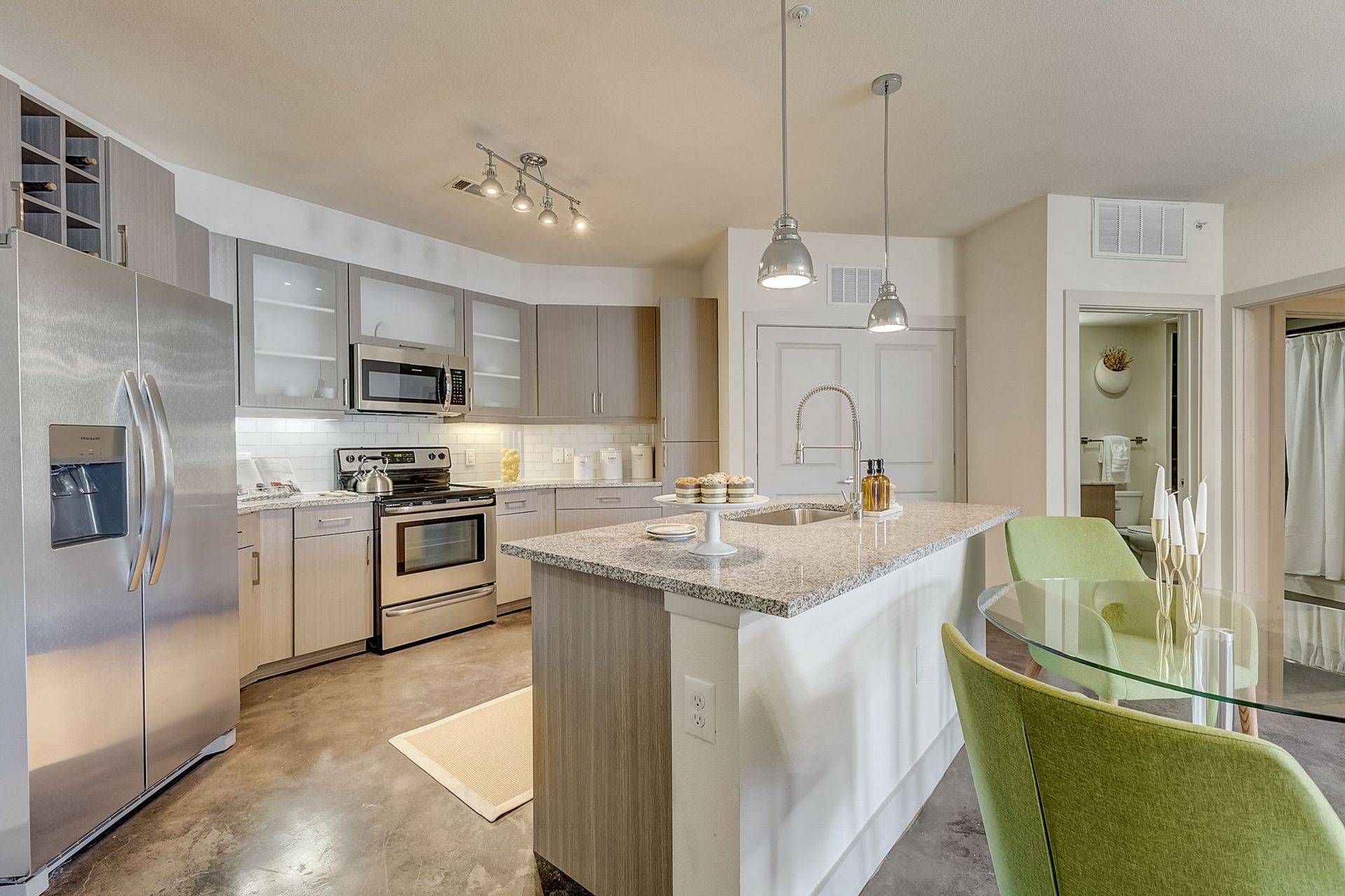 Modern kitchen with stainless steel appliances, a gray countertop, and a central island with granite and light green chairs.