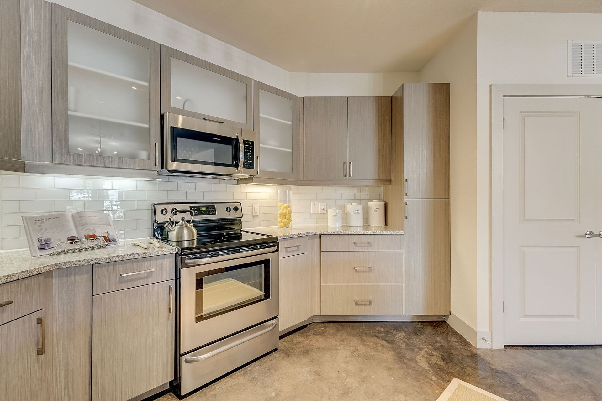 Modern kitchen with light gray cabinets, stainless steel appliances, and a white tiled backsplash.