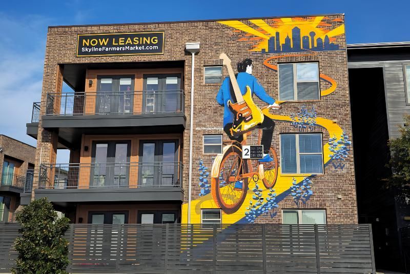Mural on a brick building depicts a musician playing guitar while riding a bicycle. The background features a city skyline.