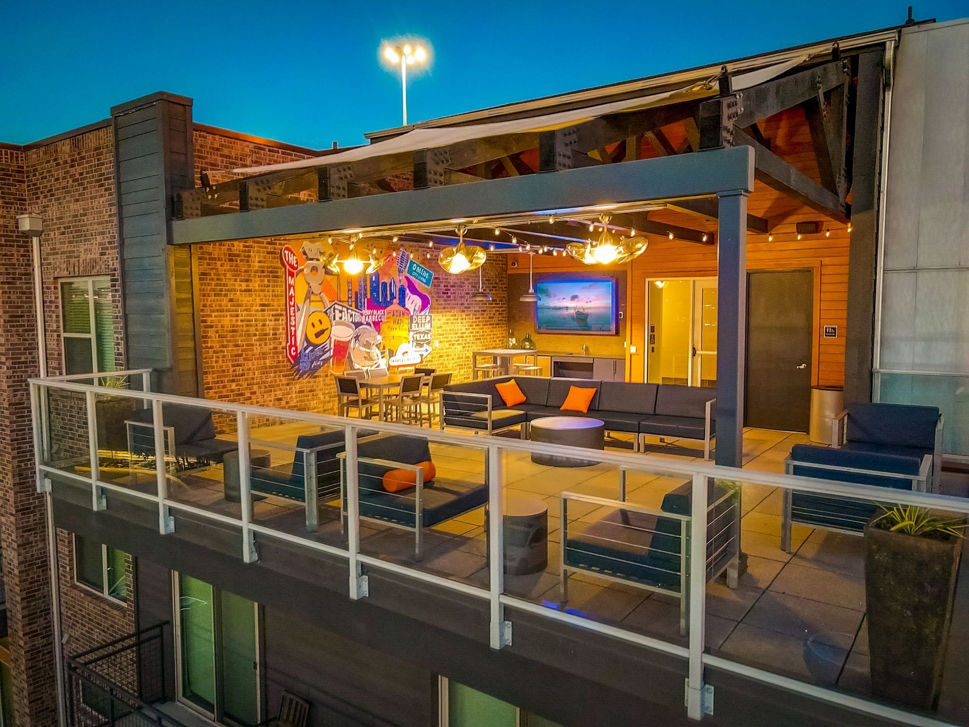 Rooftop patio with seating, bar area, and graffiti art under a wooden canopy. Evening setting with warm lighting.