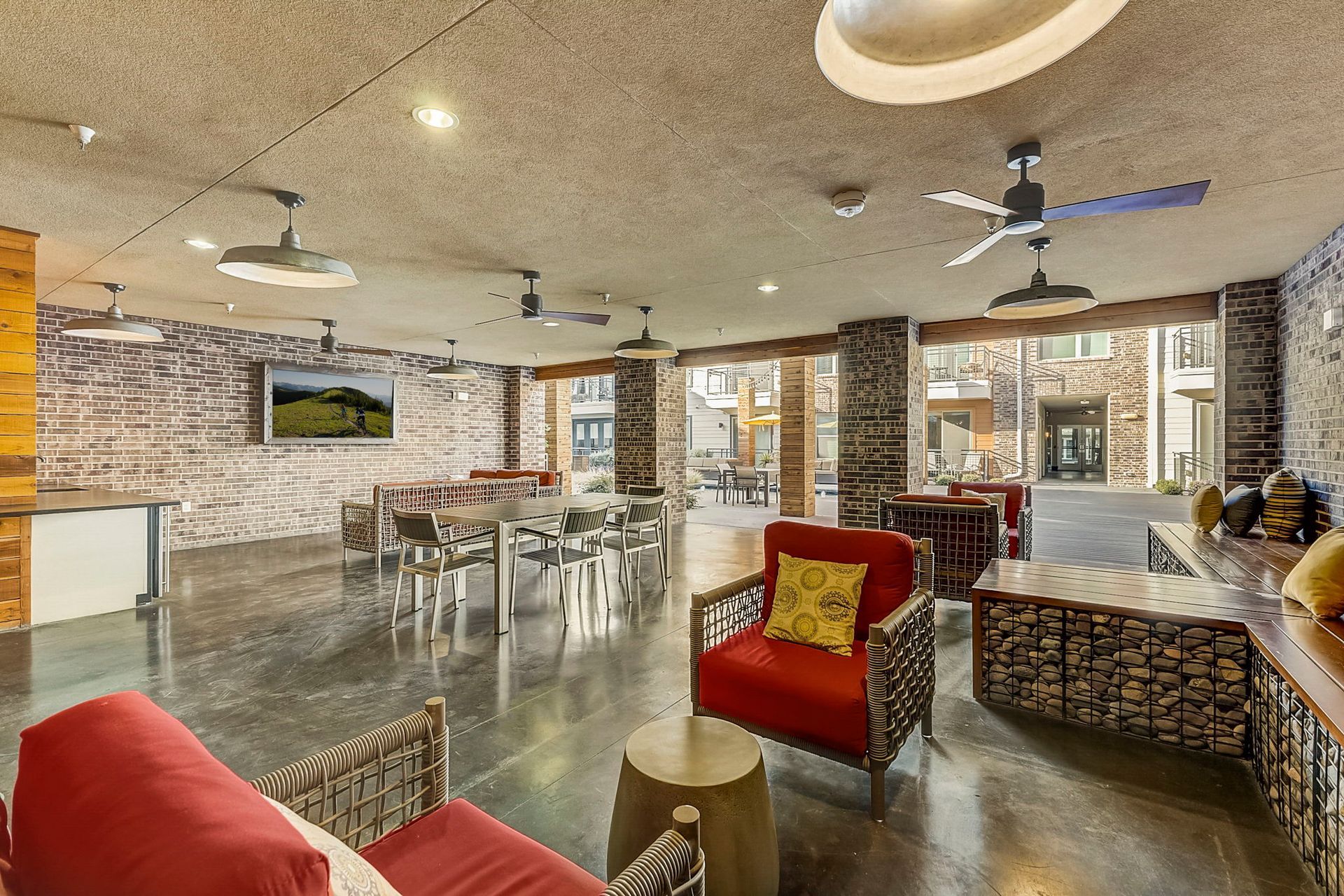 A modern lounge area with brick and stone walls, red chairs, a TV, and an outdoor patio visible through open doorways.
