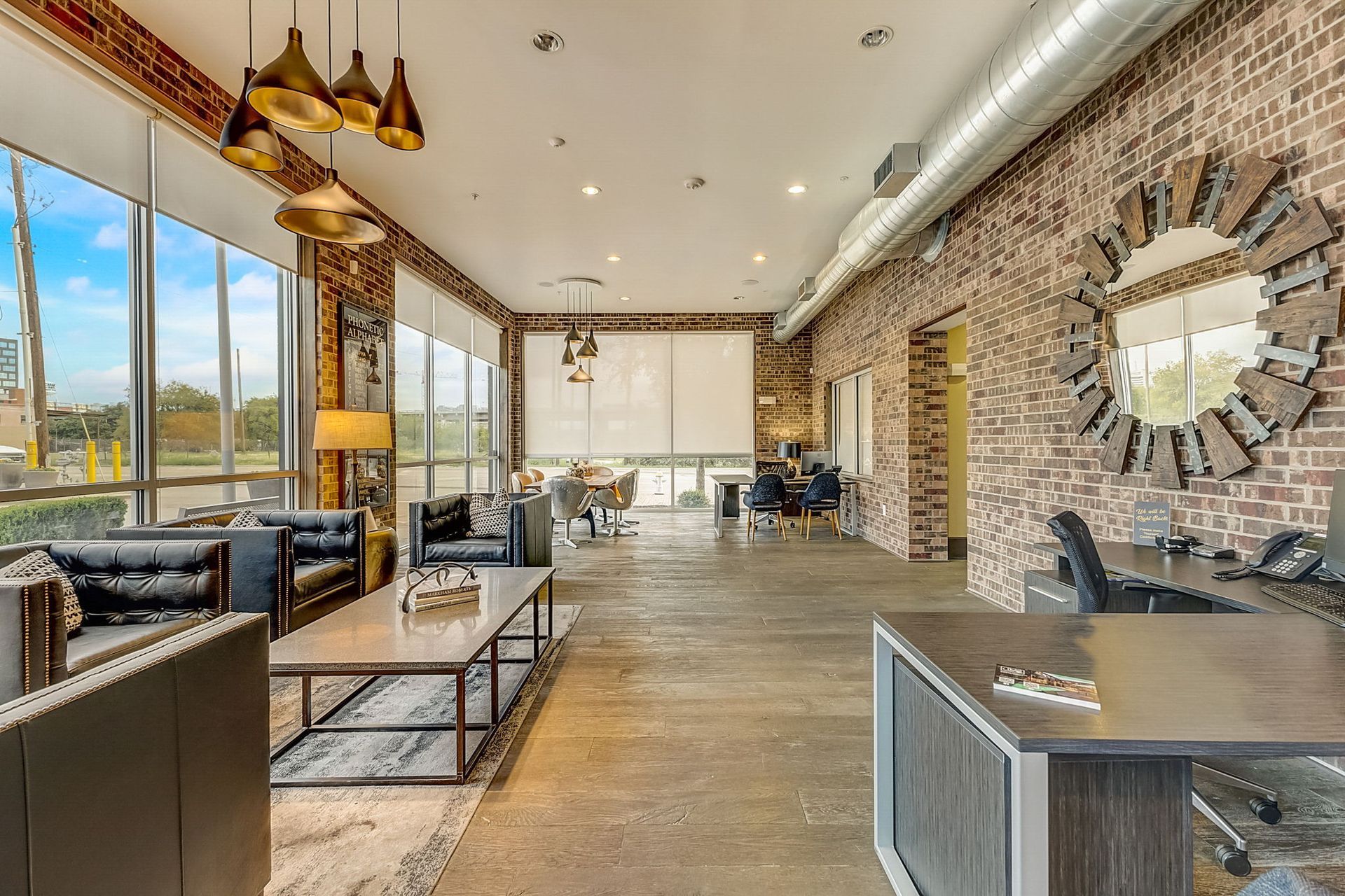 Modern office lobby with exposed brick walls, large windows, and stylish furniture.  A large mirror and gold light fixtures add to the contemporary design.