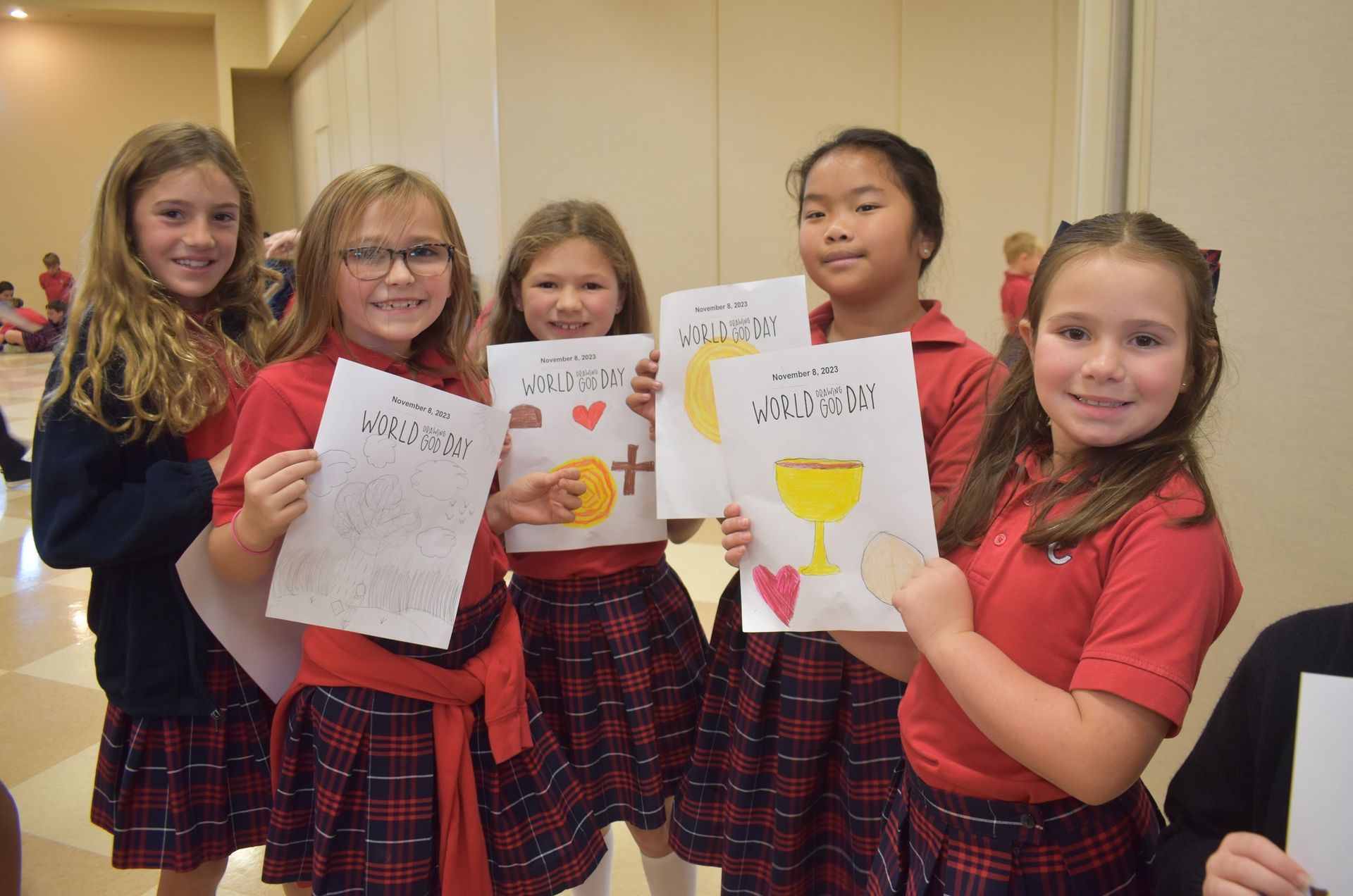 A group of young girls in red uniforms are holding up drawings