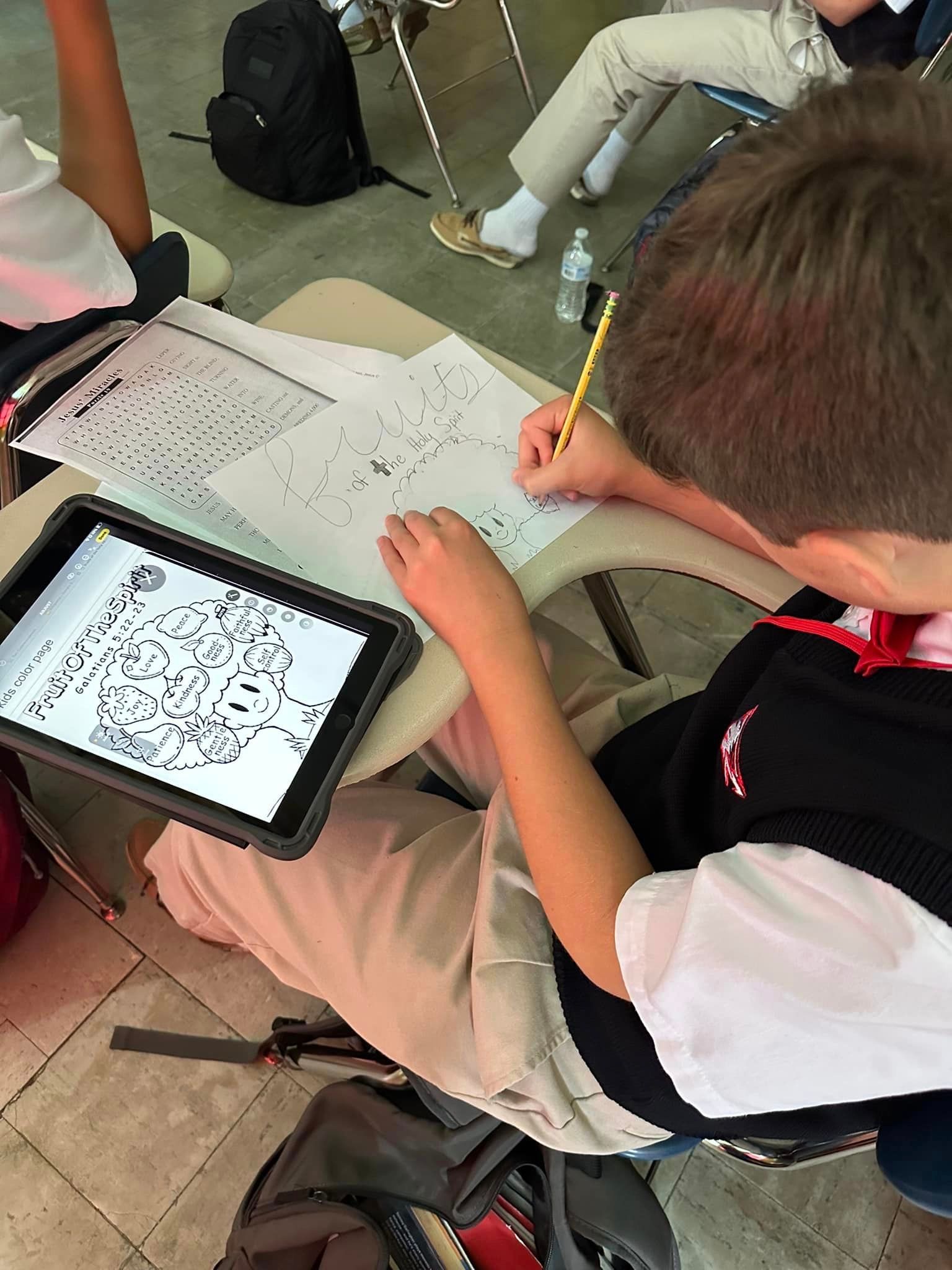 A boy sits at a desk with a tablet and a pencil