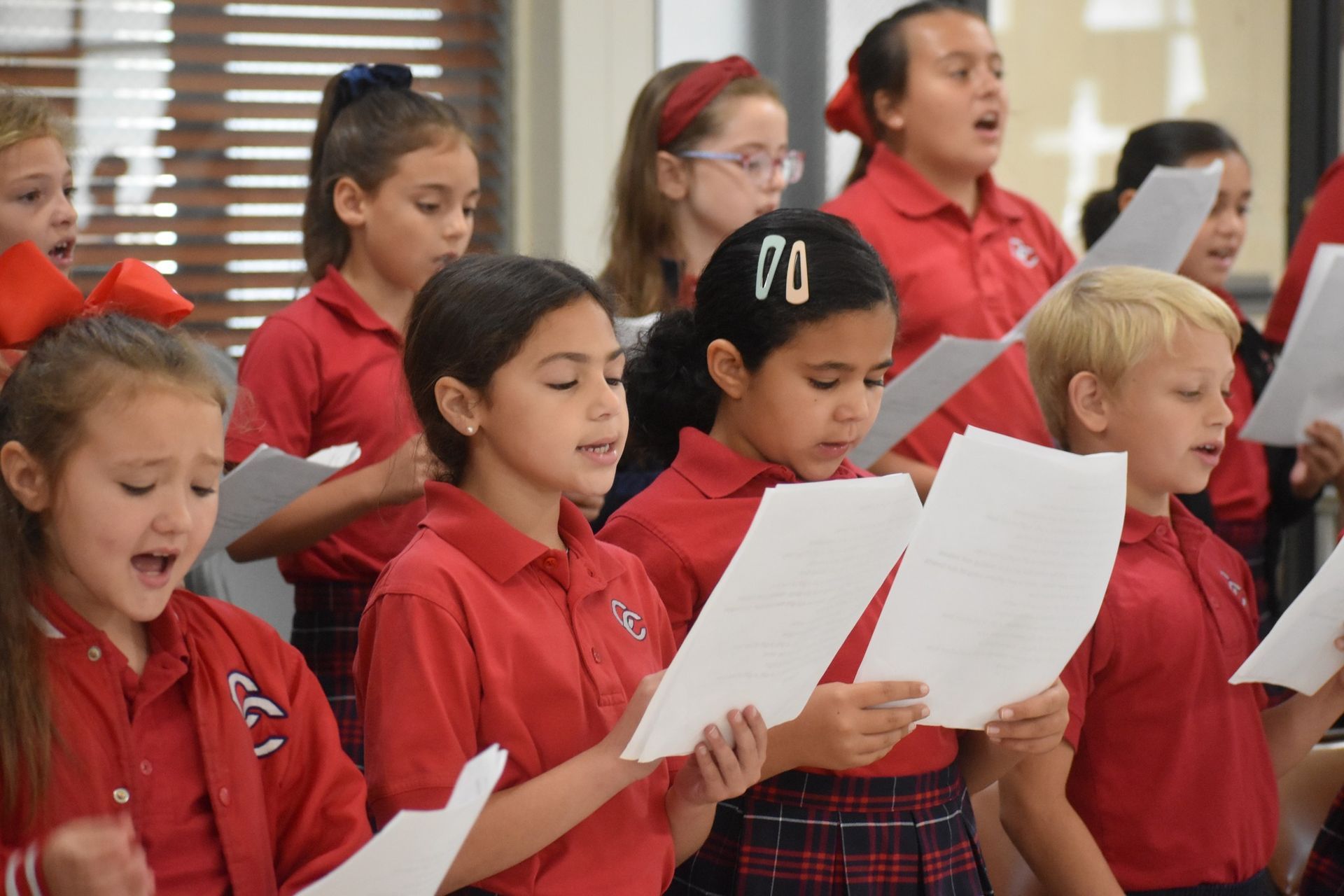 A group of children in red uniforms are singing together