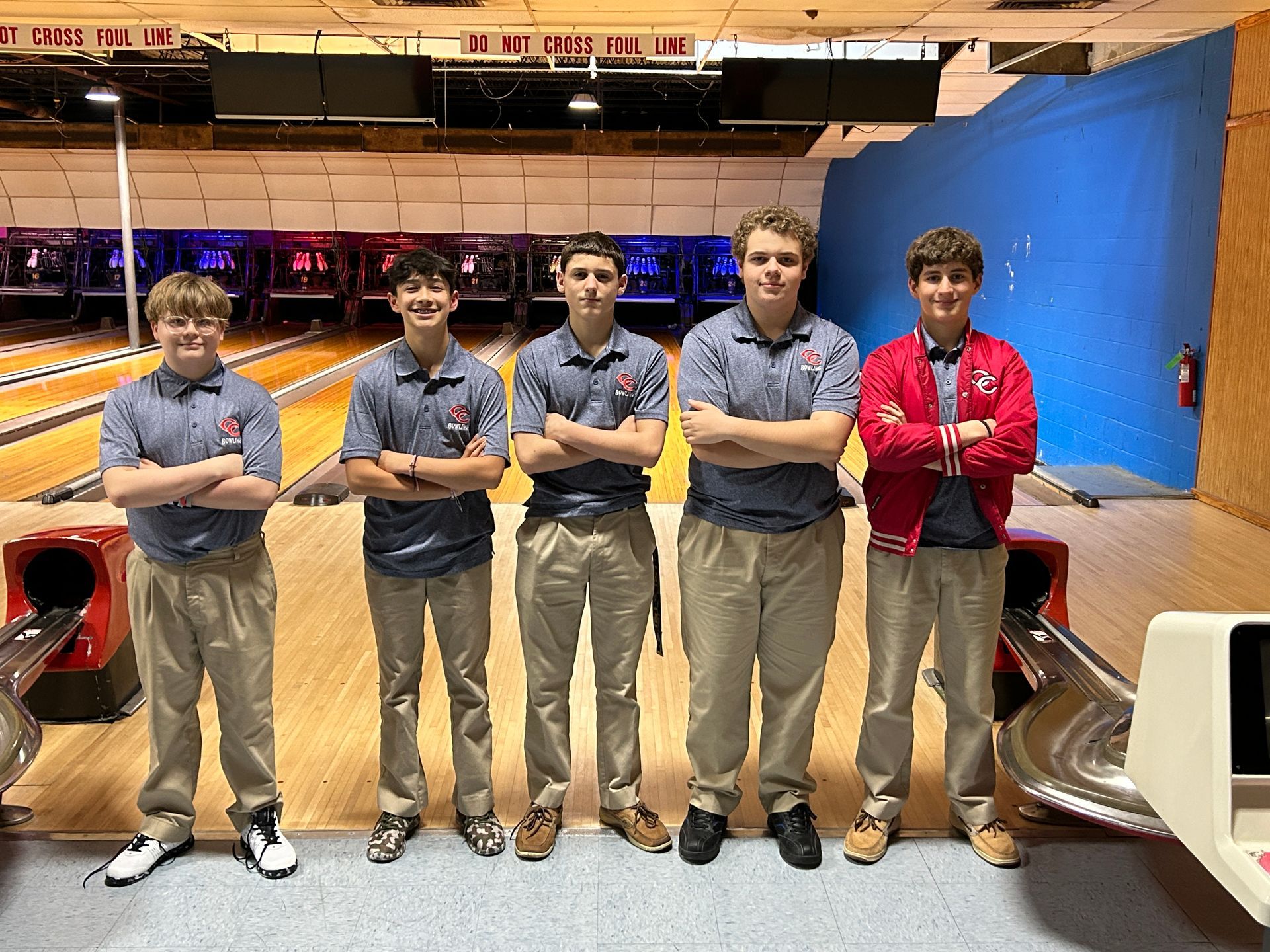 A group of young men standing in a bowling alley with their arms crossed