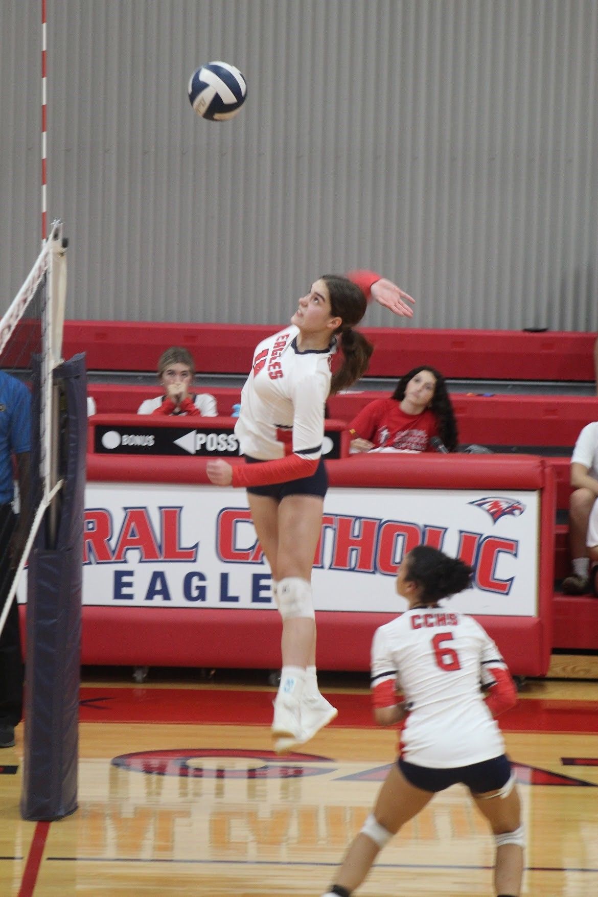 A volleyball player jumps to hit the ball in front of a sign that says eagle