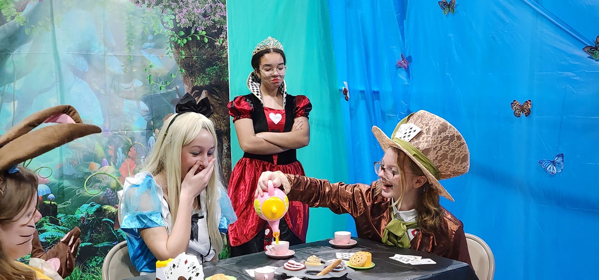 A group of children dressed in alice in wonderland costumes are having a tea party