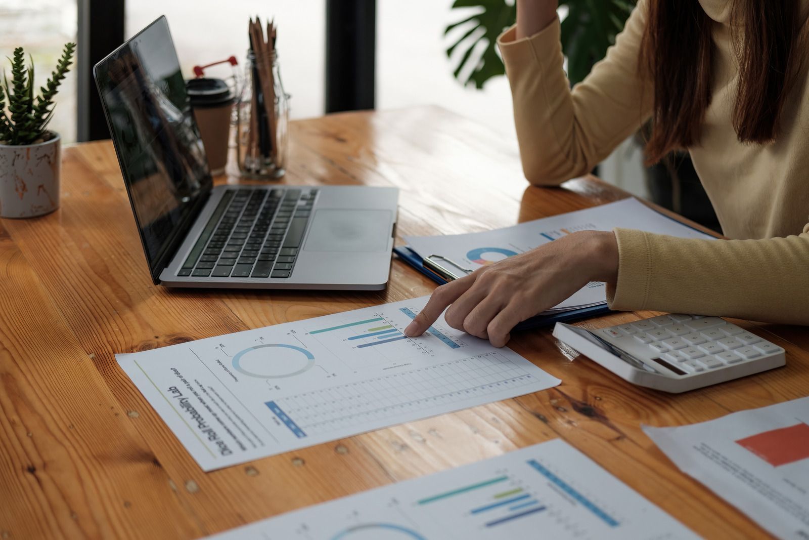 Woman pointing to a chart with a laptop and calculator on a wooden desk.
