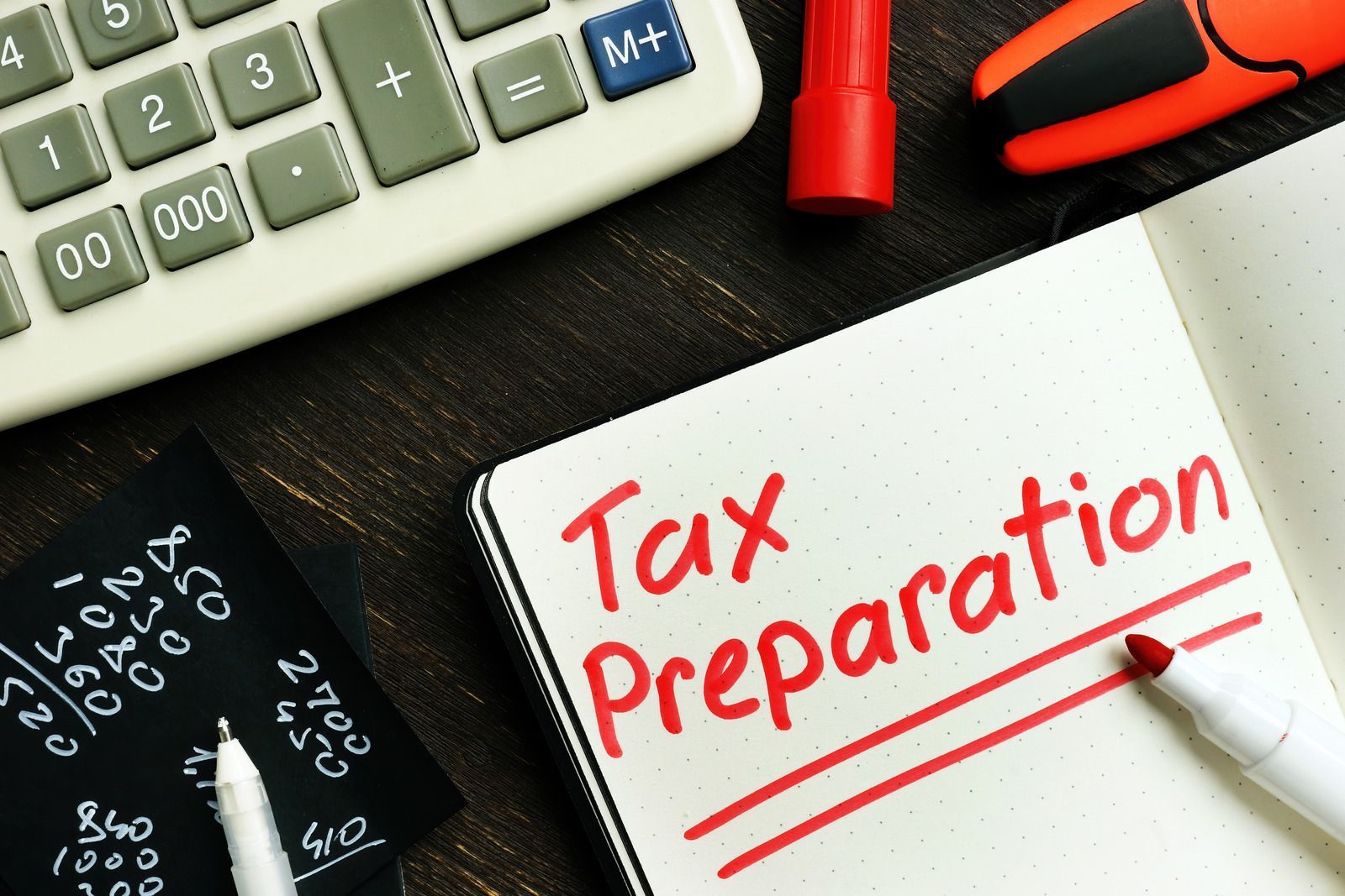 Tax preparation: calculator, notepad with text, red marker, numbers on a black board.