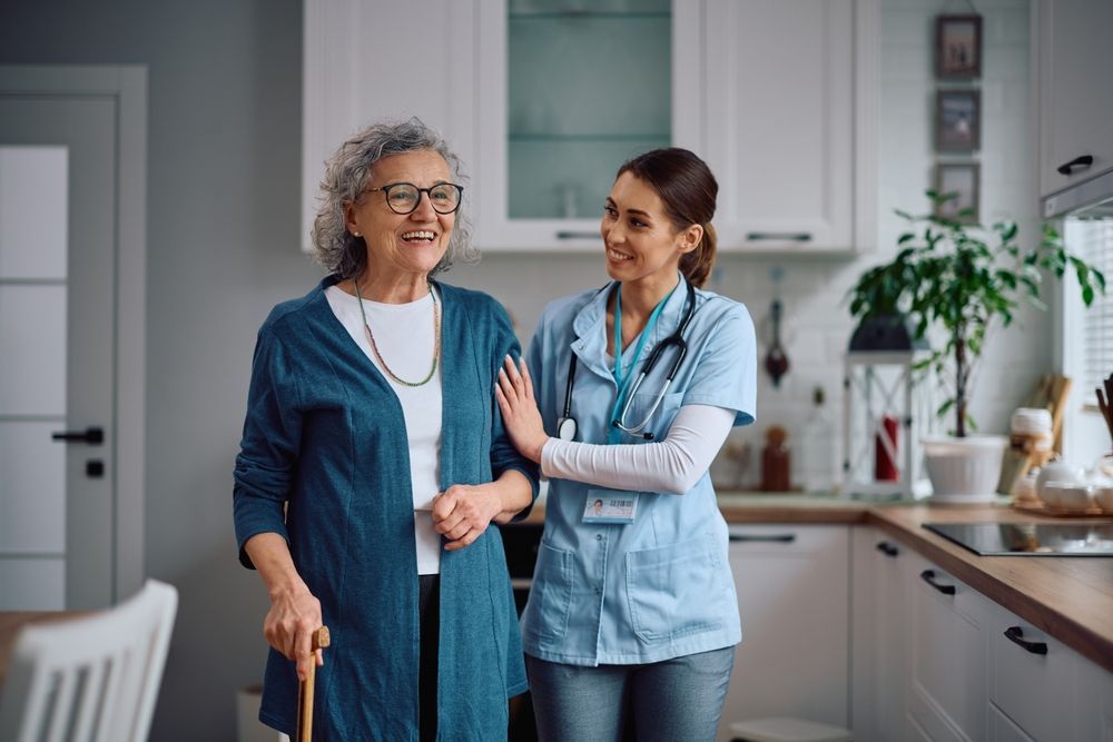 Happy home caregiver assisting her senior patient with walking through the kitchen.