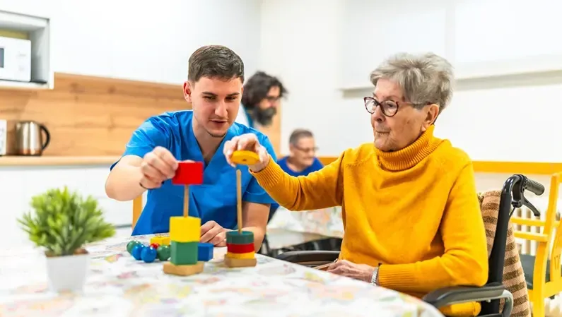 Caregiver and elderly person playing with colorful blocks.