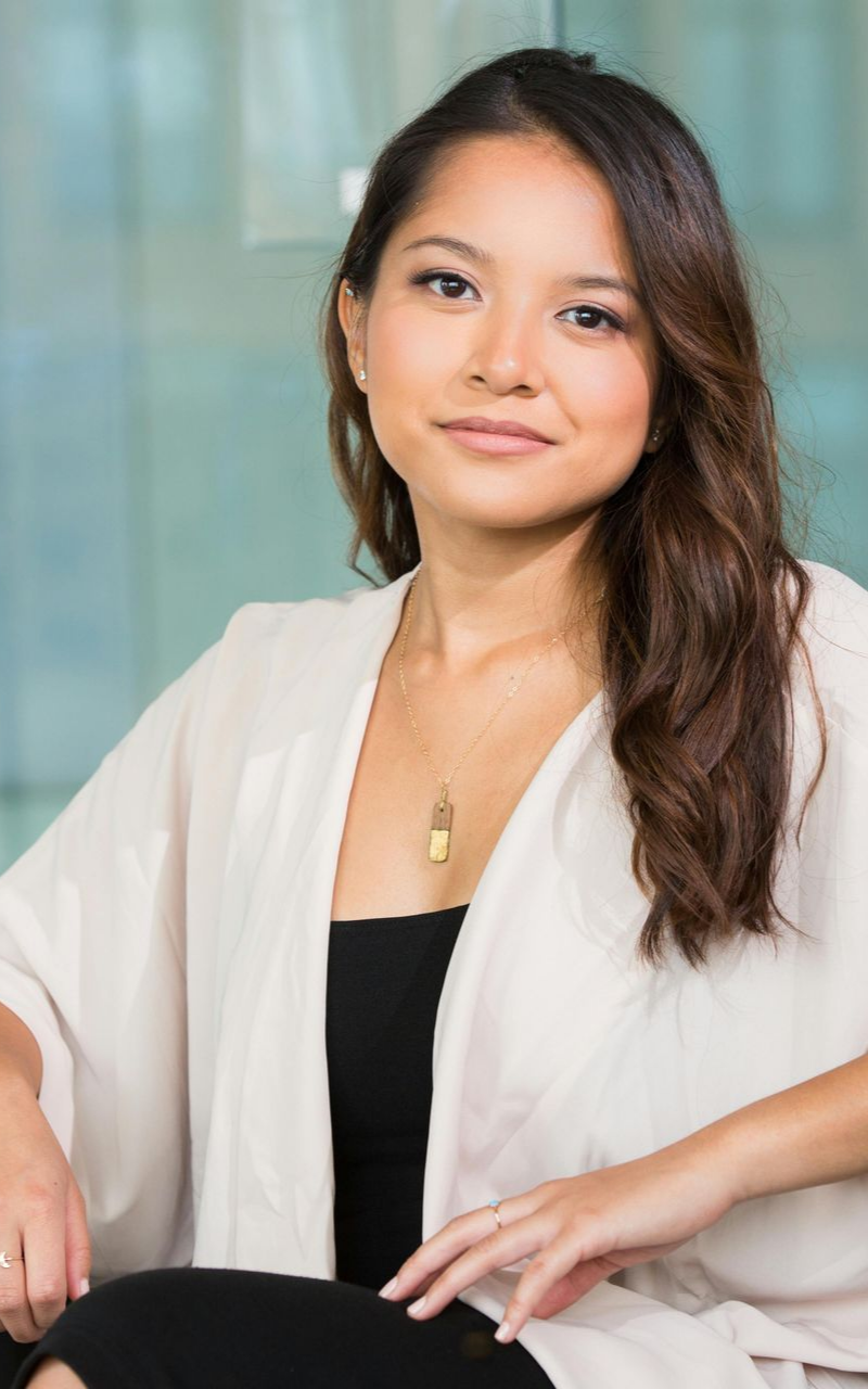 Woman with brown hair in a light sweater, seated indoors, smiling.