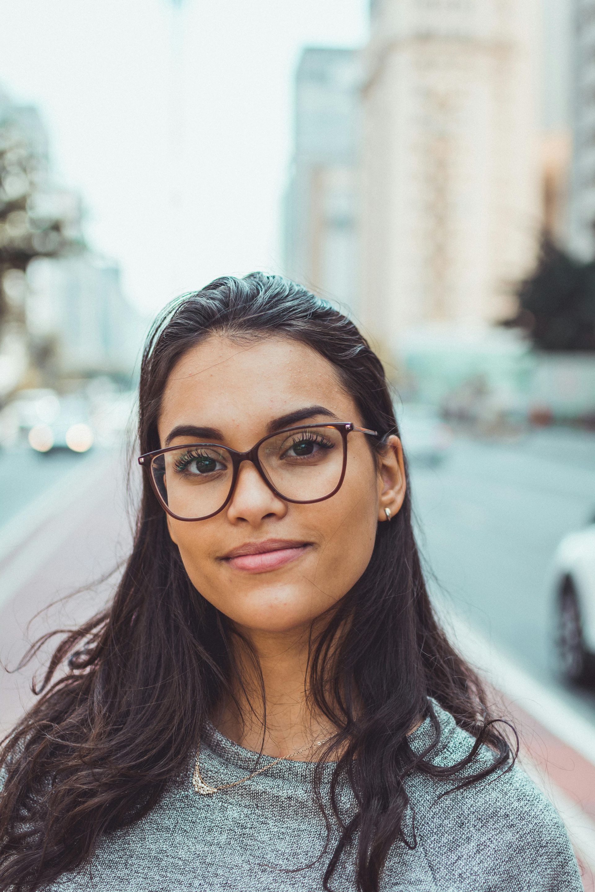 Woman with glasses smiling on a city street.