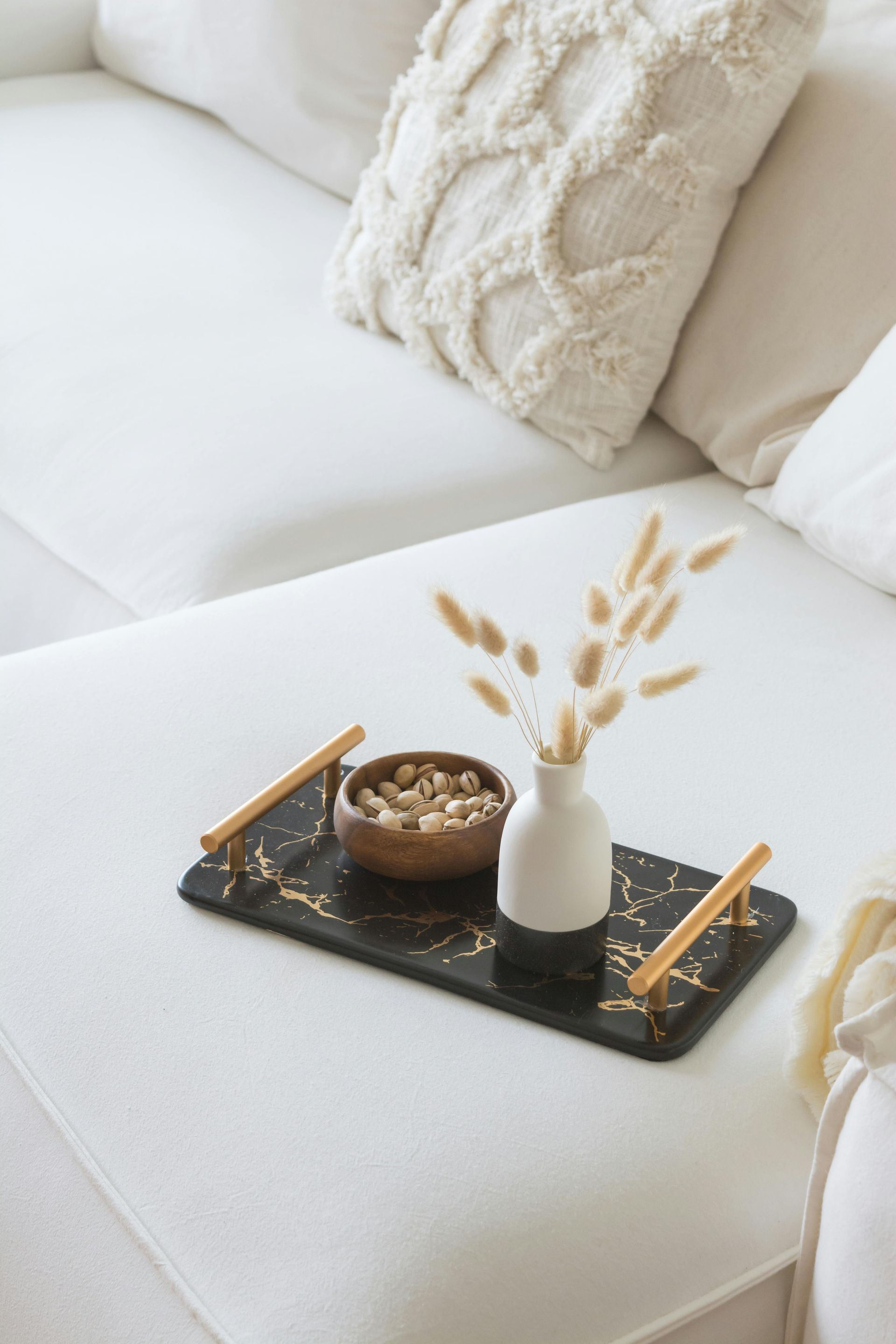 White couch with a black tray holding snacks and vase with dried flowers.