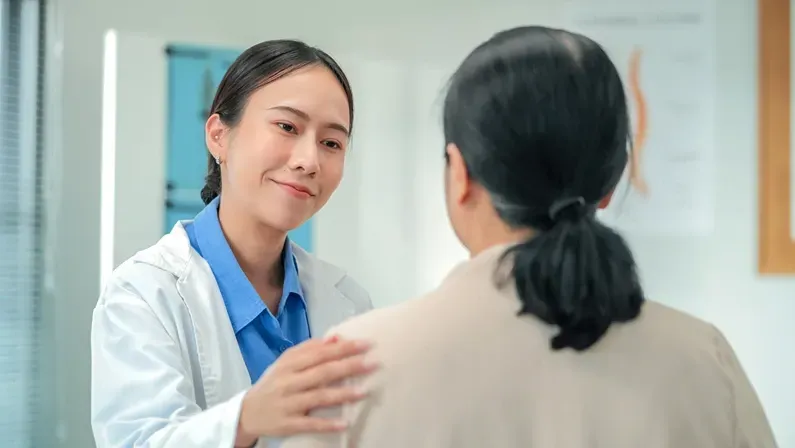 Happy Asian female doctor demonstrates compassionate care, holding hands with senior patient. Therapeutic touch approach showcases empathetic healthcare delivery and patient-centered emotional support