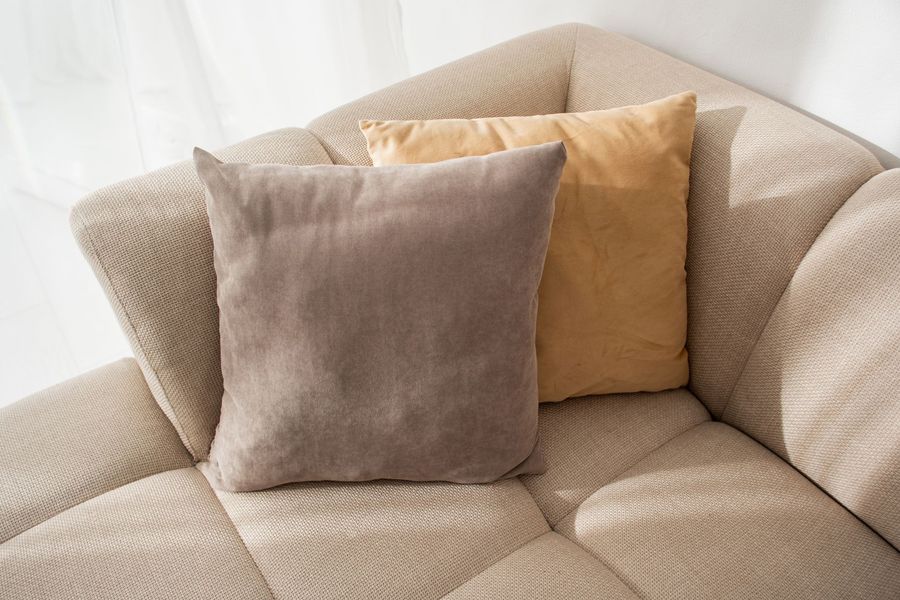 Two throw pillows, brown and gold, on a beige sectional sofa.