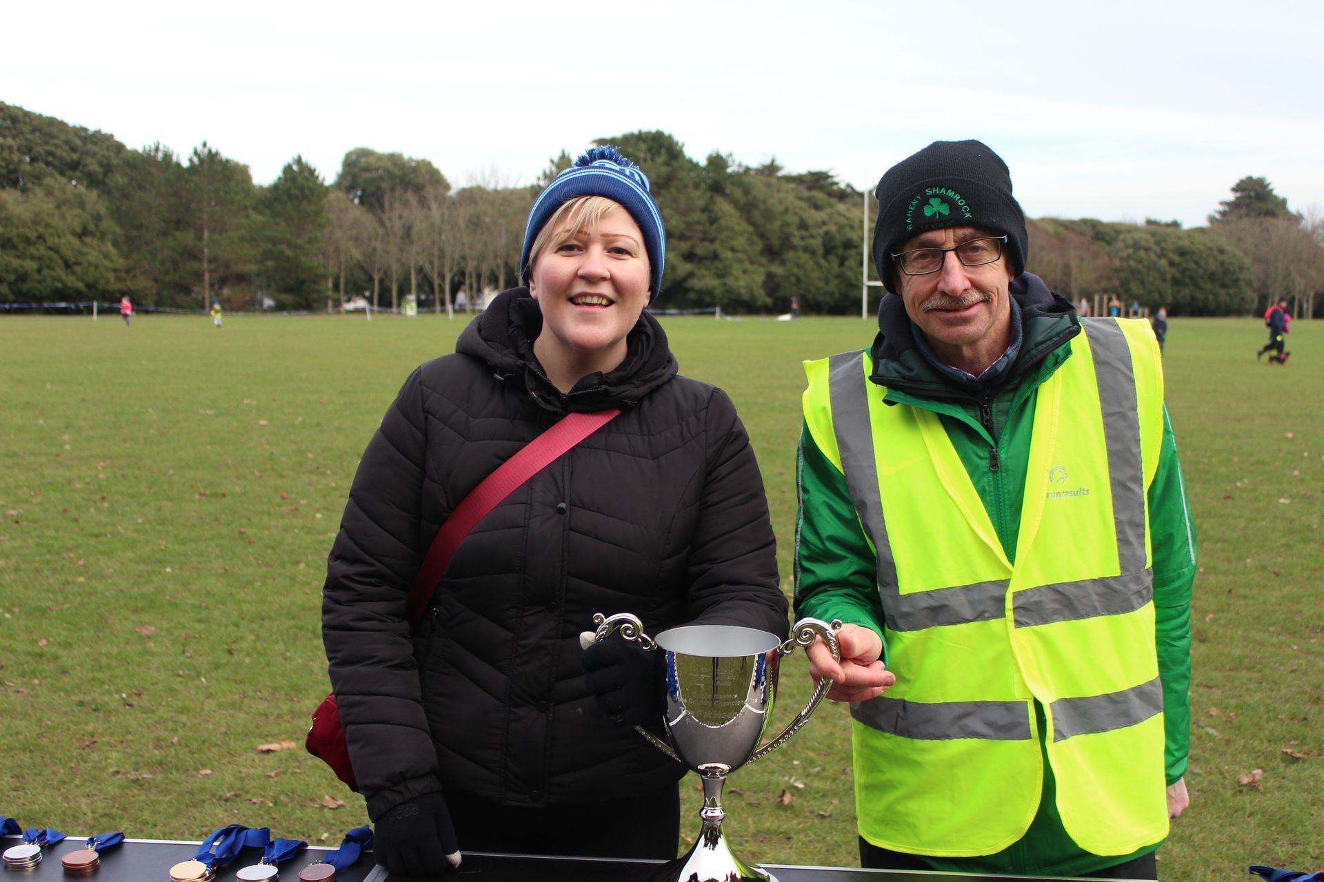 A man and a woman are holding a trophy in a field.