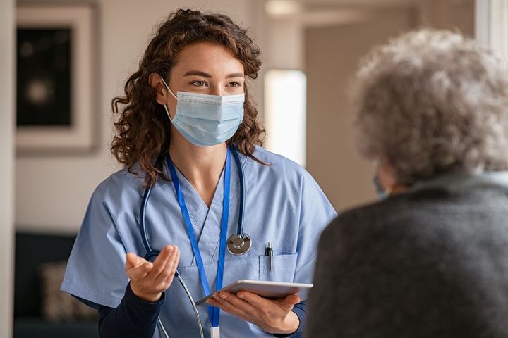 a nurse wearing a mask is talking to an elderly woman .
