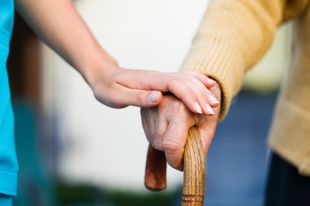 a nurse is holding the hand of an elderly woman holding a cane .