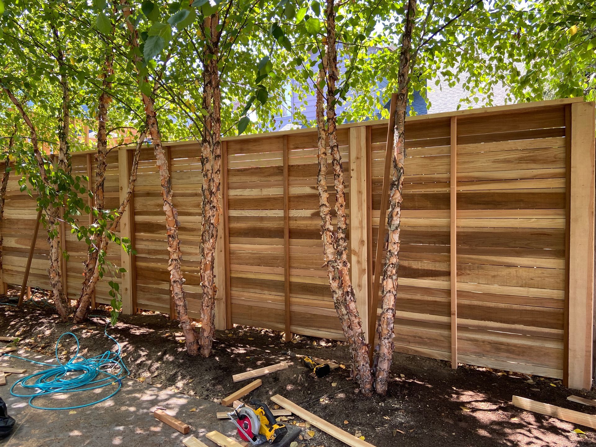 A wooden fence is being built in a backyard surrounded by trees.