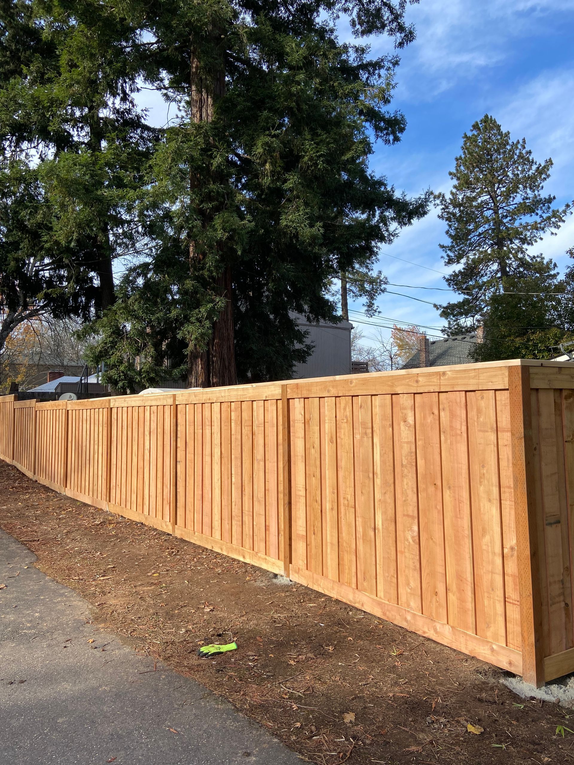 A wooden fence along a sidewalk with trees in the background.