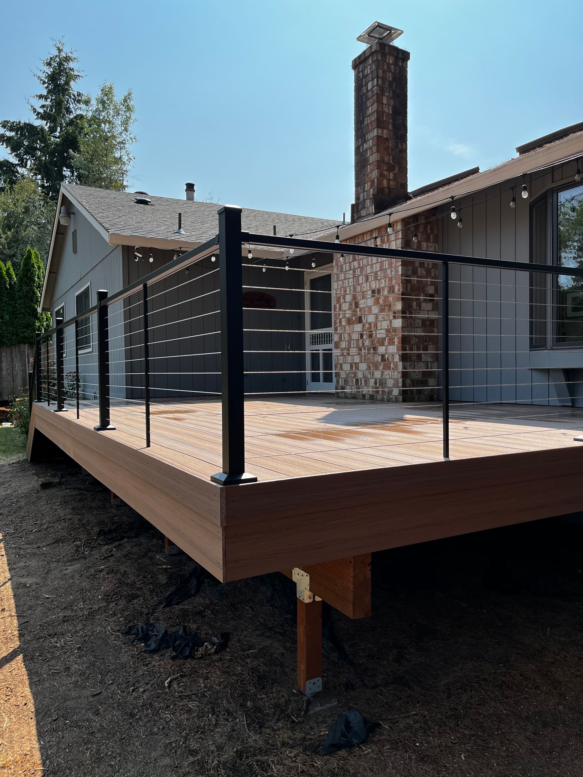 A wooden deck with a black railing is in front of a house.