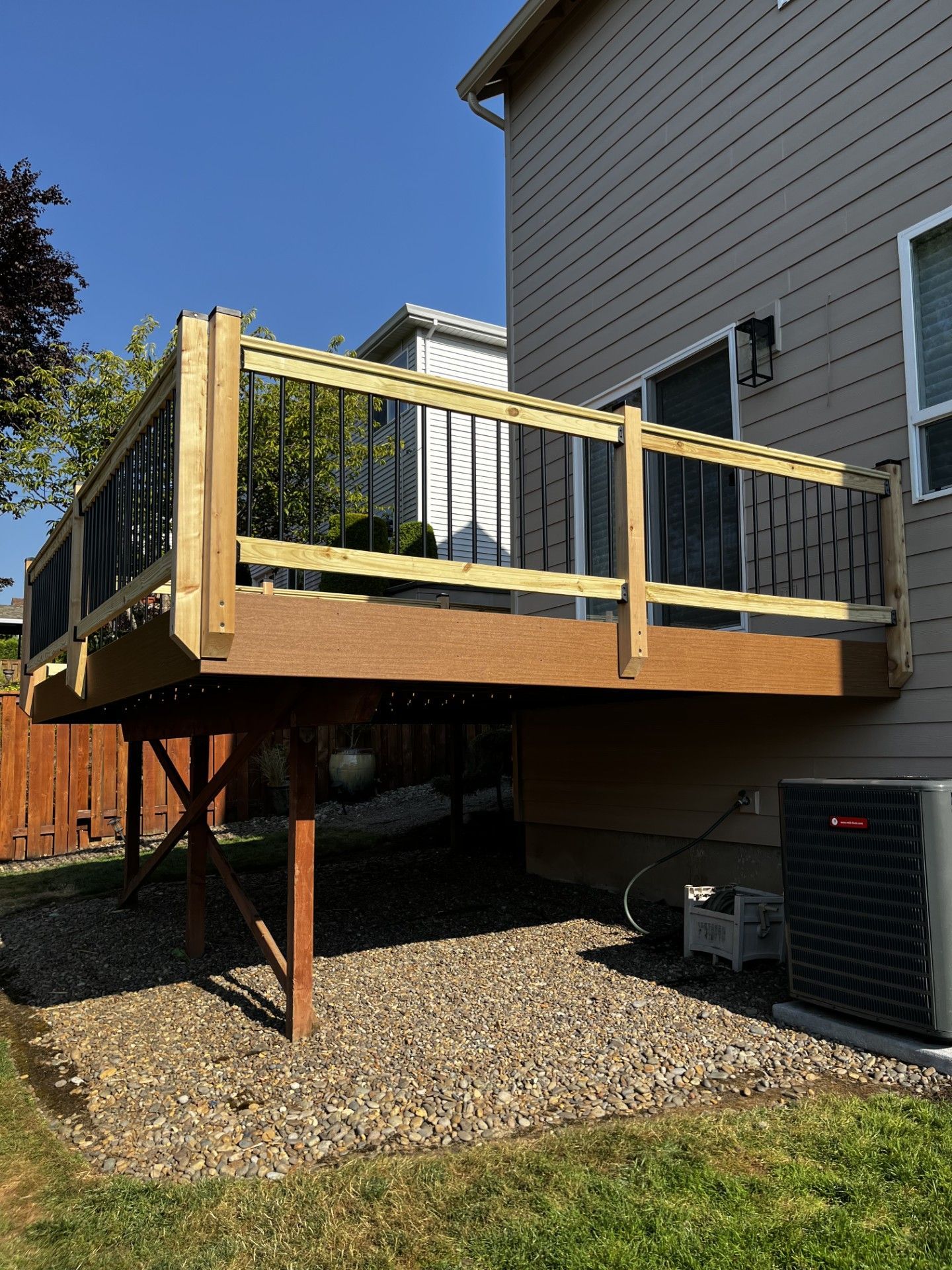 A wooden deck with a metal railing is in the backyard of a house.