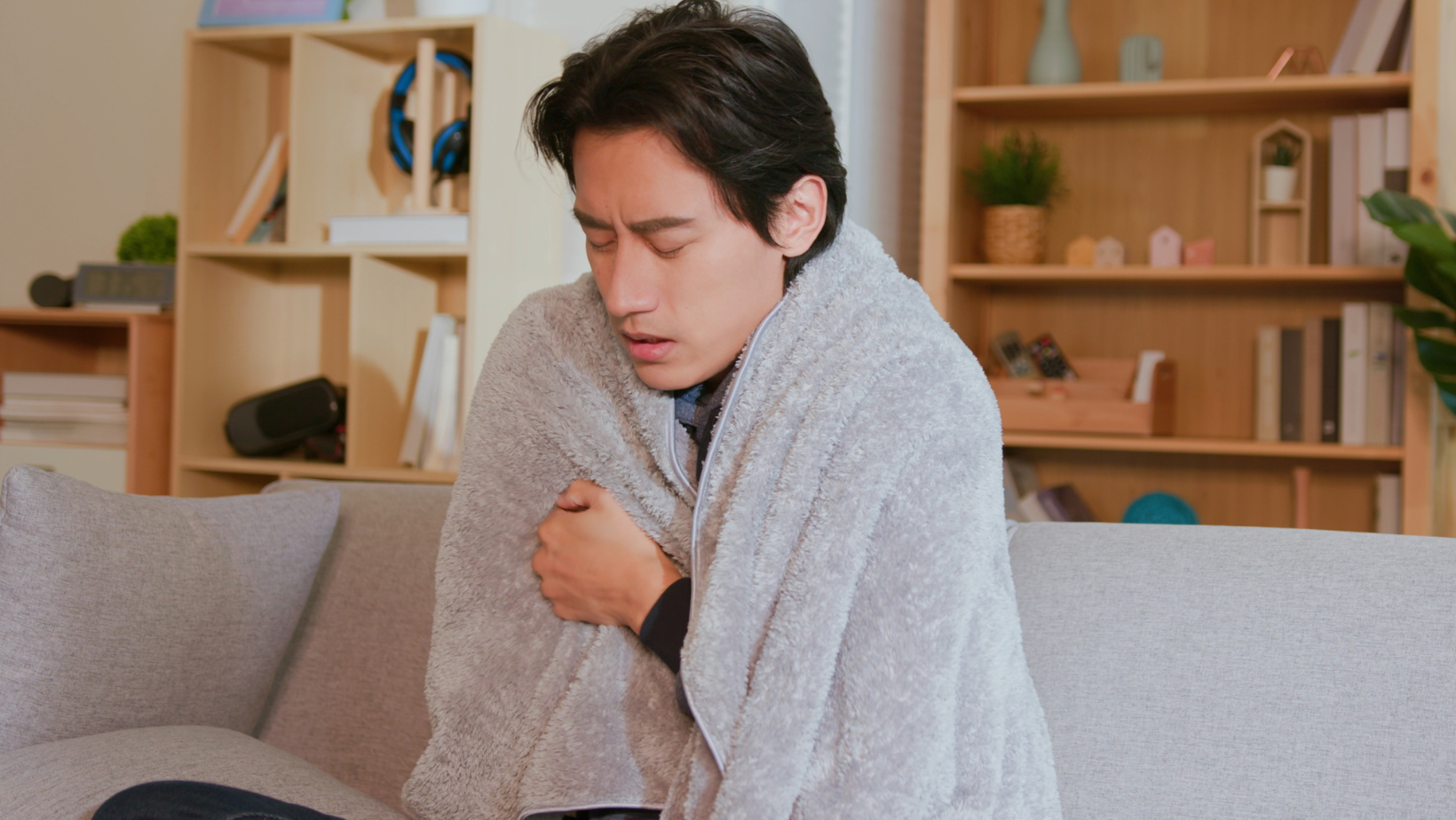 A man is sitting on a couch wrapped in a blanket.