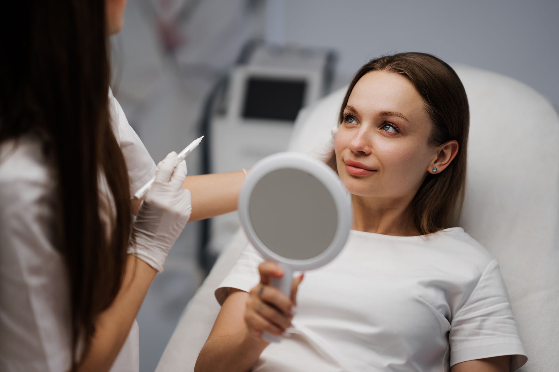 A woman is sitting in a chair looking at herself in a mirror.