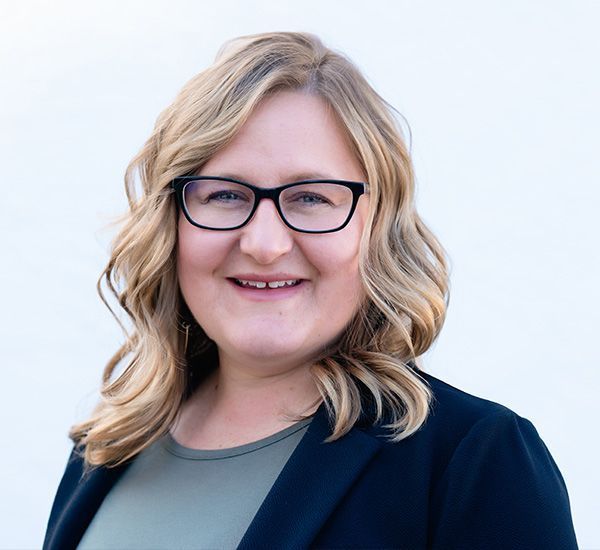 A woman wearing glasses and a black jacket is smiling for the camera.