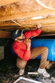 A man in a red shirt and blue hat is kneeling down in front of a house.