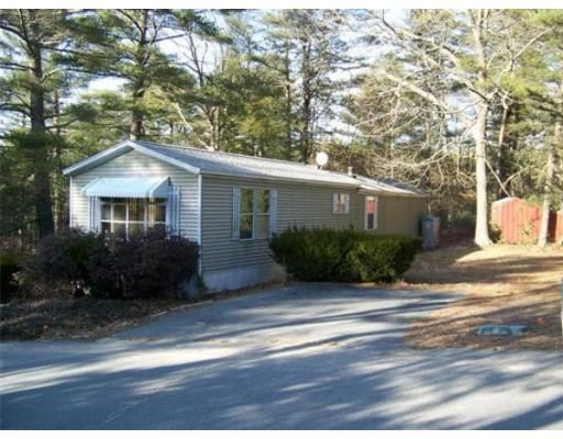A small house with a driveway and trees in the background