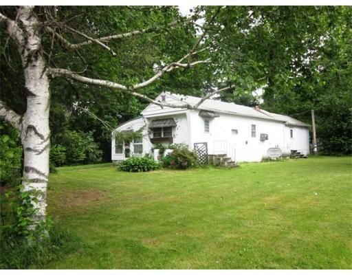 A white house sits in the middle of a lush green field surrounded by trees.