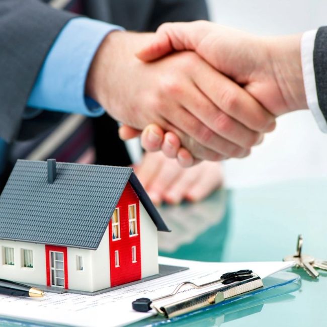 Two people shaking hands over a model house on a clipboard