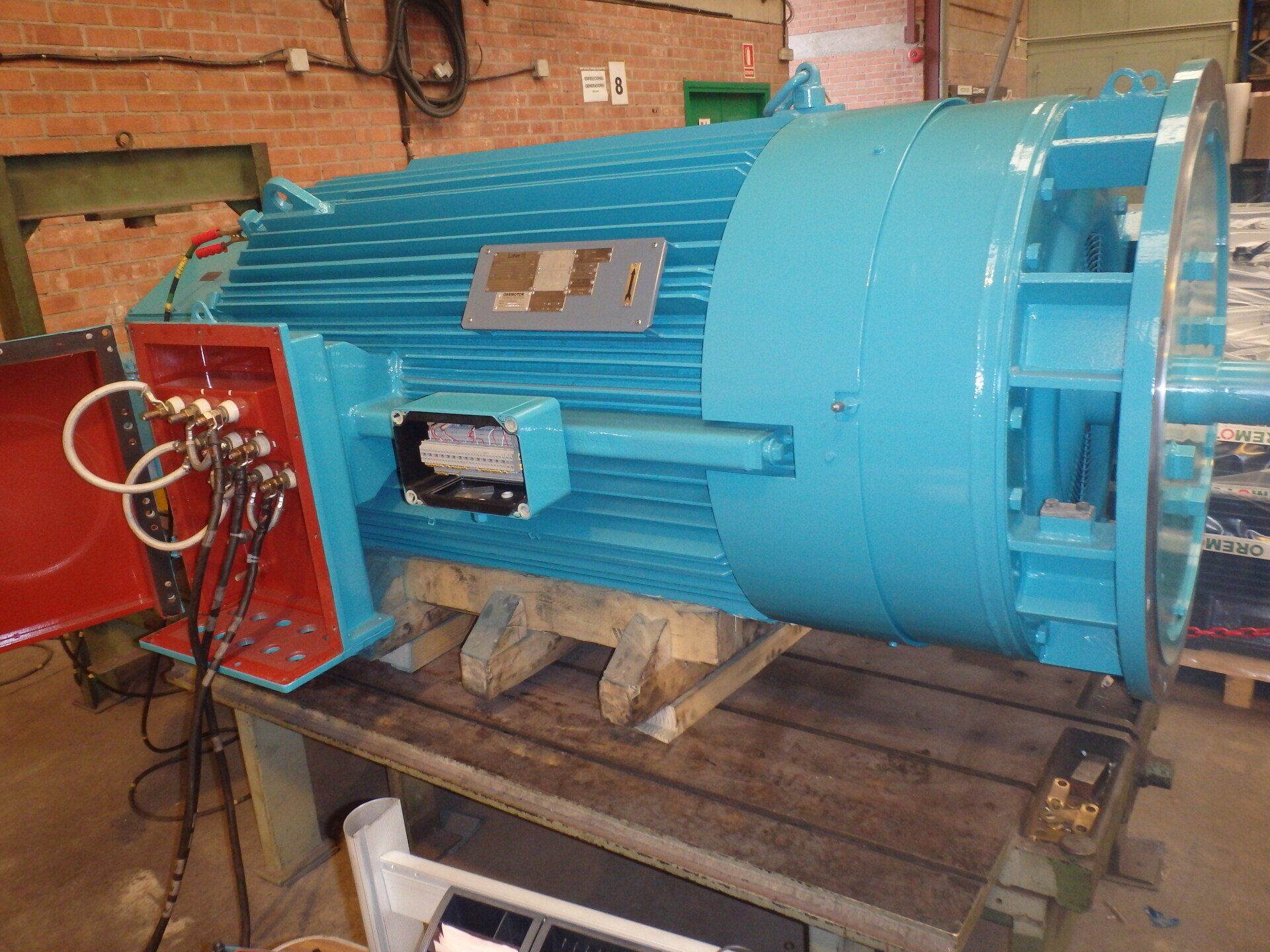 Gran motor eléctrico industrial de color turquesa sobre un soporte de madera en un entorno de taller.