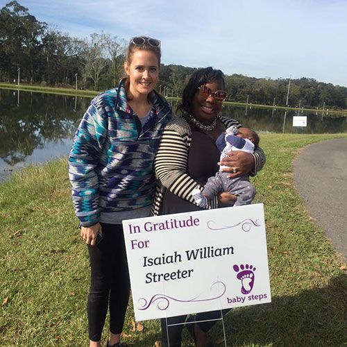 Two women and a baby by a lake holding a sign that says