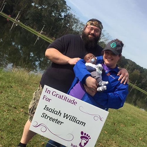Couple holding baby by a lake; woman holding sign that reads