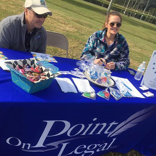 Two people at a Point On Legal booth. A table with freebies, pens, and brochures.