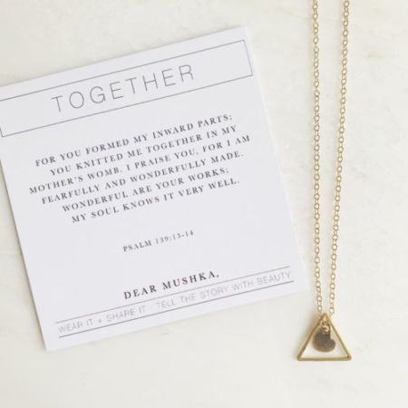 Necklace with a gold chain and a triangle pendant; next to a card with the word 