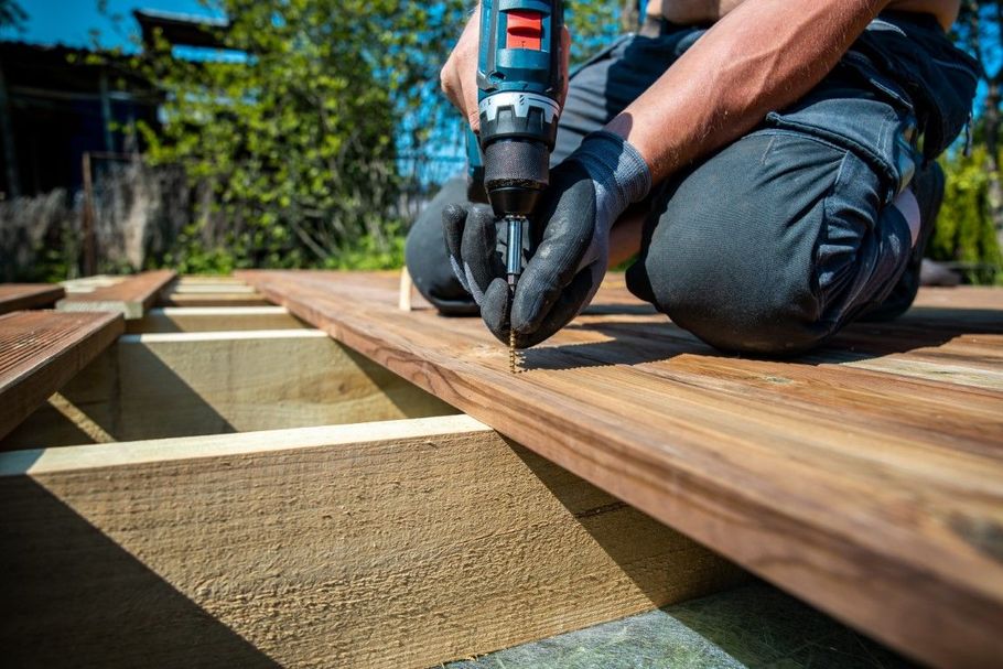 Person using a power drill to fasten wooden deck boards outdoors